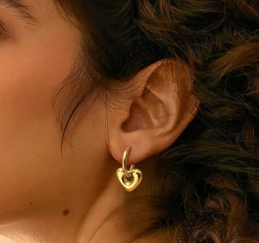 A pair of gold-colored stainless steel hoop earrings with a textured surface in ear
