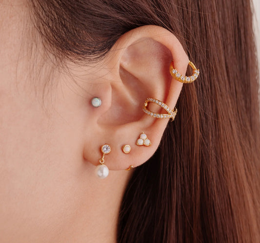 A pair of gold-colored hoop earrings with white opal stones set in them in ear