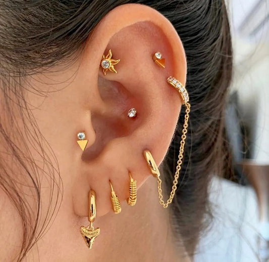 A double gold-colored stud earring with a clear gemstone in ear.