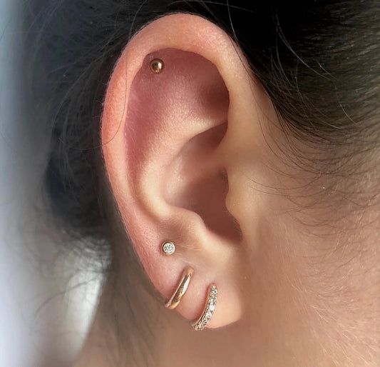 A pair of gold-colored stainless steel ball stud earrings in ear