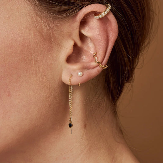 A pair of gold-colored stainless steel hoop earrings with pearl accents in ear