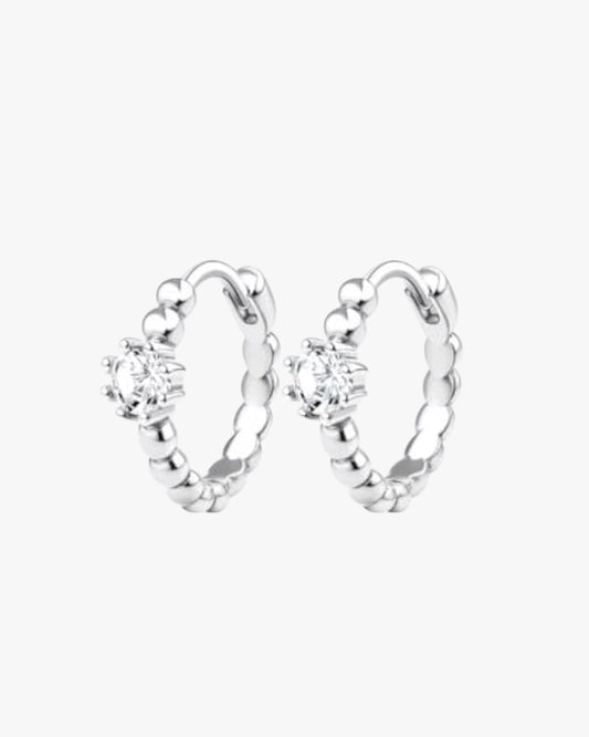 A pair of silver-colored hoop earrings with a small circular embellishment at the top, displayed against a white background.