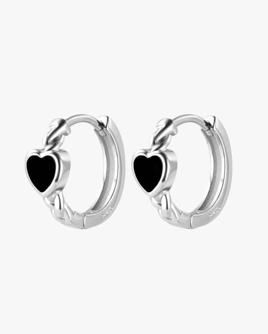 A pair of silver-colored hoop earrings with black heart-shaped details on the hoops.