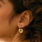 A pair of gold-colored stainless steel hoop earrings with a textured surface in ear