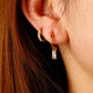 Close-up of an ear wearing gold hoop earrings with clear gemstones.