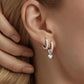 A pair of silver-colored sterling silver earrings with a heart-shaped diamond in the center, displayed in ear
