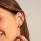 Close-up of a person wearing gold earrings and rings on a neutral background