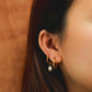 Close-up of an ear wearing gold hoop earrings with a pearl earring against a warm-toned background.