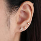 A gold-colored stainless steel heart-shaped stud with a small clear crystal in the center, attached to a gold-plated cap and bar in ear