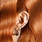Close-up of an ear with multiple earrings against a background of wavy red hair.