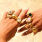 Close-up of a hand wearing multiple gold rings with various gemstones on a beige background