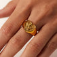Gold heart-shaped ring on a person's finger against a white background