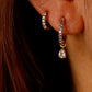 Close-up of an ear wearing gold hoop earrings with clear gemstones.
