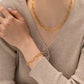 Person wearing a gold chain necklace and bracelet against a neutral background