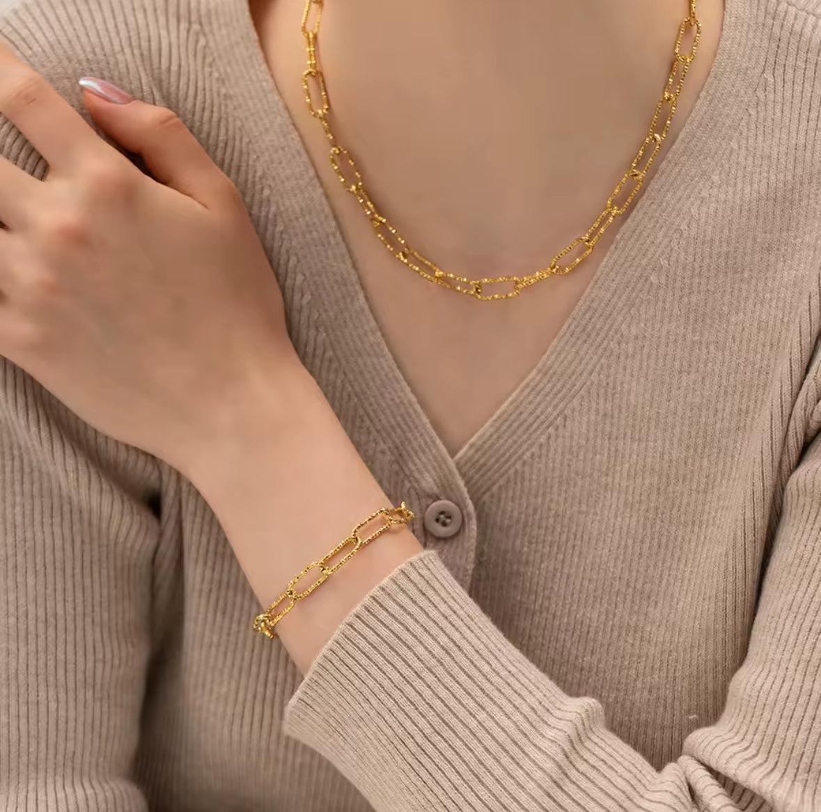 Person wearing a gold chain necklace and bracelet against a neutral background