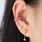 A pair of gold-colored stainless steel earrings with a geometric design, featuring three spherical elements connected by a central point in ear
