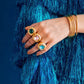 Hand wearing gold rings with gemstones against a blue textured background