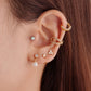 A pair of gold-colored hoop earrings with white opal stones set in them in ear