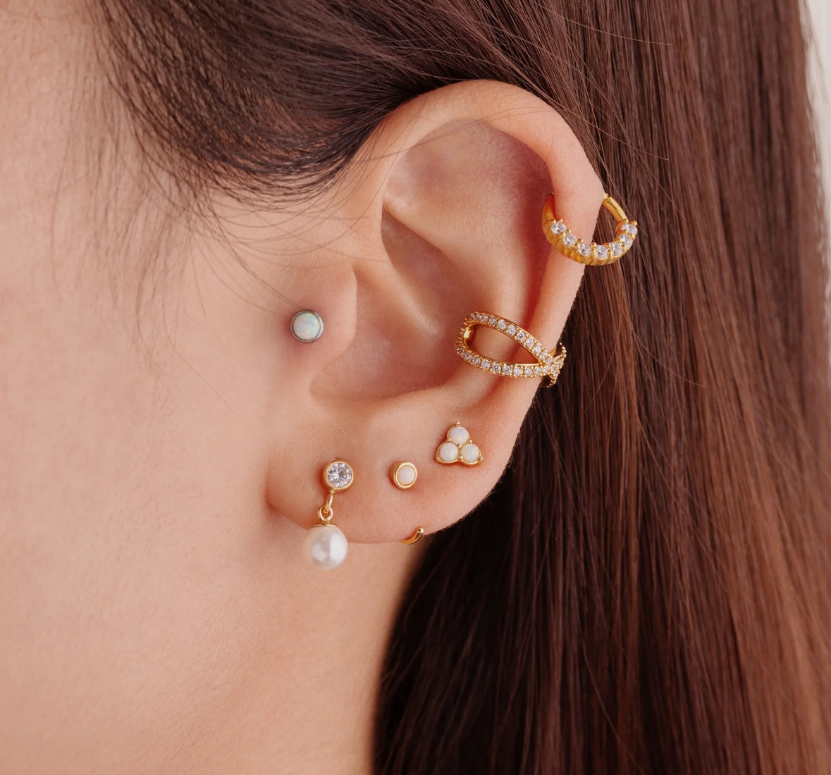 A pair of gold-colored hoop earrings with white opal stones set in them in ear