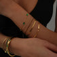 Close-up of a wrist wearing multiple gold bracelets with green gemstones on a dark background