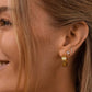 Close-up of a woman's ear wearing gold hoop earrings with a neutral background