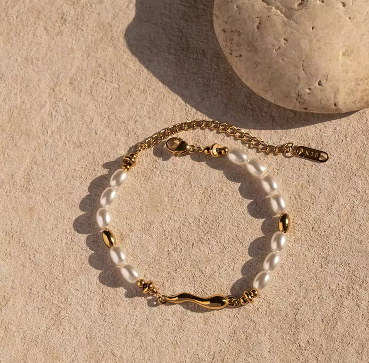Pearl bracelet with gold accents on a beige stone surface