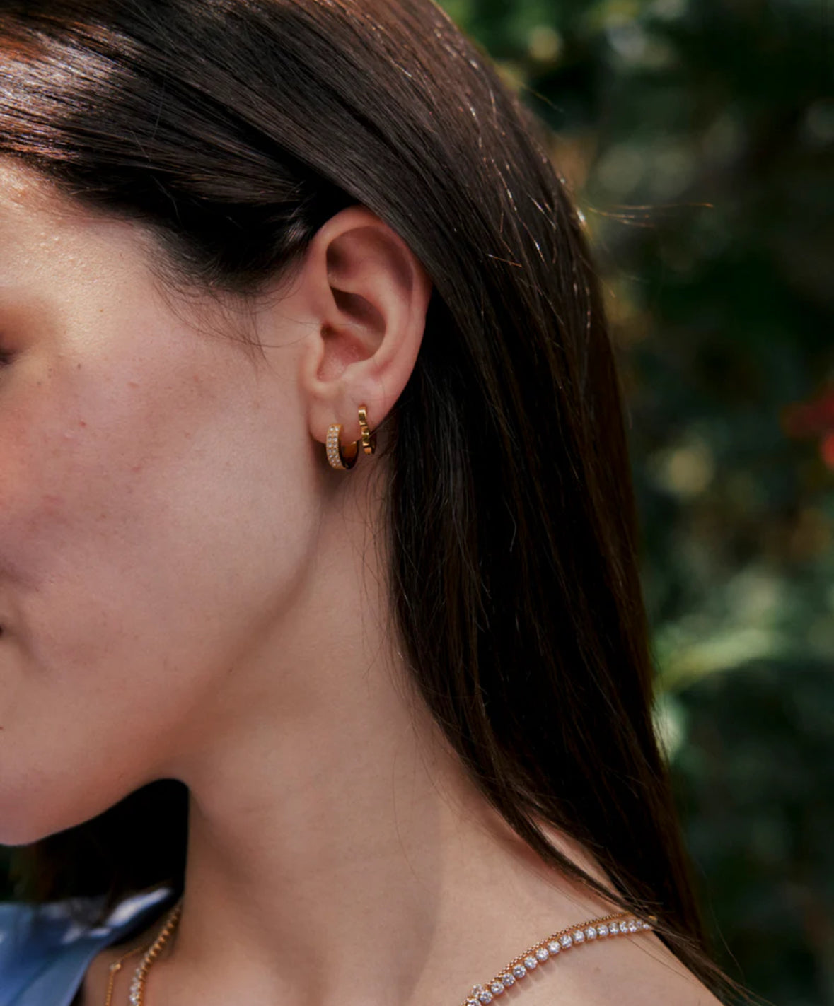Close-up of a person wearing gold hoop earrings with a blurred green background