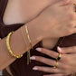 Gold bracelets and rings on a person's wrist and hand against a brown background