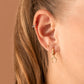 A pair of gold-colored hoop earrings with a textured surface in ear