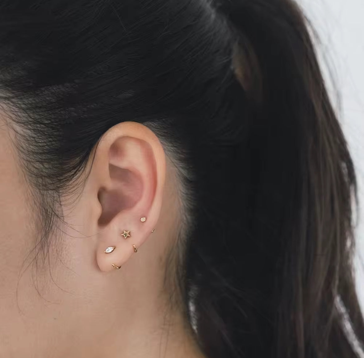 Close-up of an ear with gold earrings against a neutral background