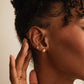 A gold-colored clicker hoop earring with a chain design in ear