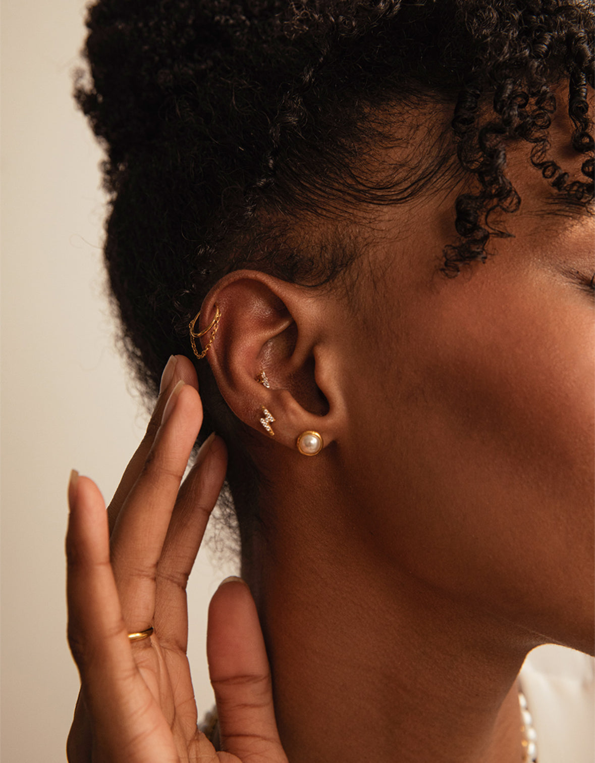 A gold-colored clicker hoop earring with a chain design in ear