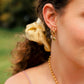 Close-up of a person wearing gold earrings and a necklace with a blurred natural background