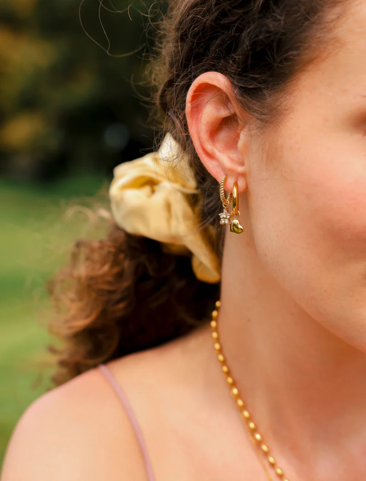 Close-up of a person wearing gold earrings and a necklace with a blurred natural background