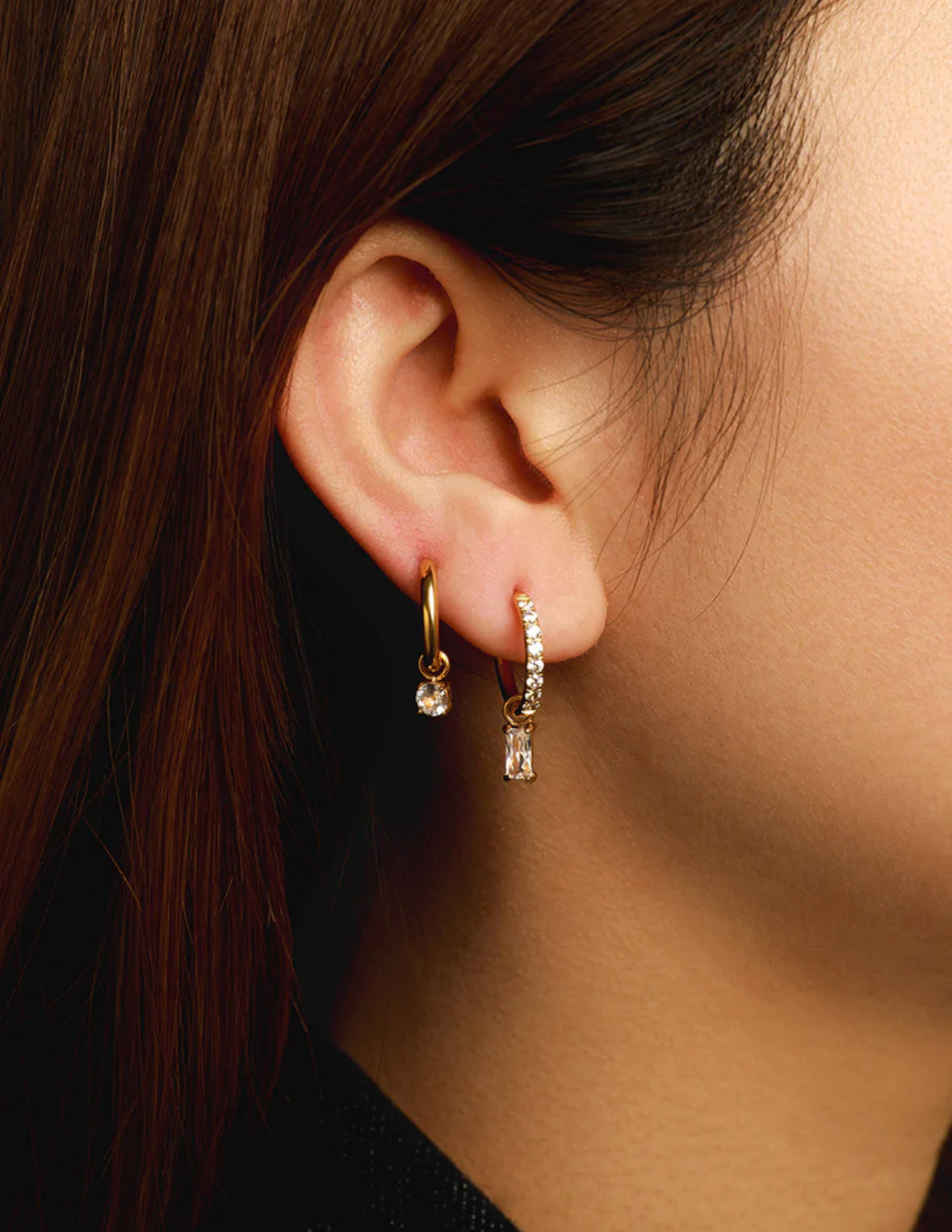 Close-up of an ear wearing gold hoop earrings with small crystals.