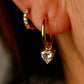 Gold hoop earrings with heart-shaped gemstones worn on an ear.