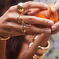 Close-up of hands with gold rings holding a peach against a blurred background