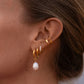 Close-up of an ear wearing gold hoop earrings with a pearl earring.