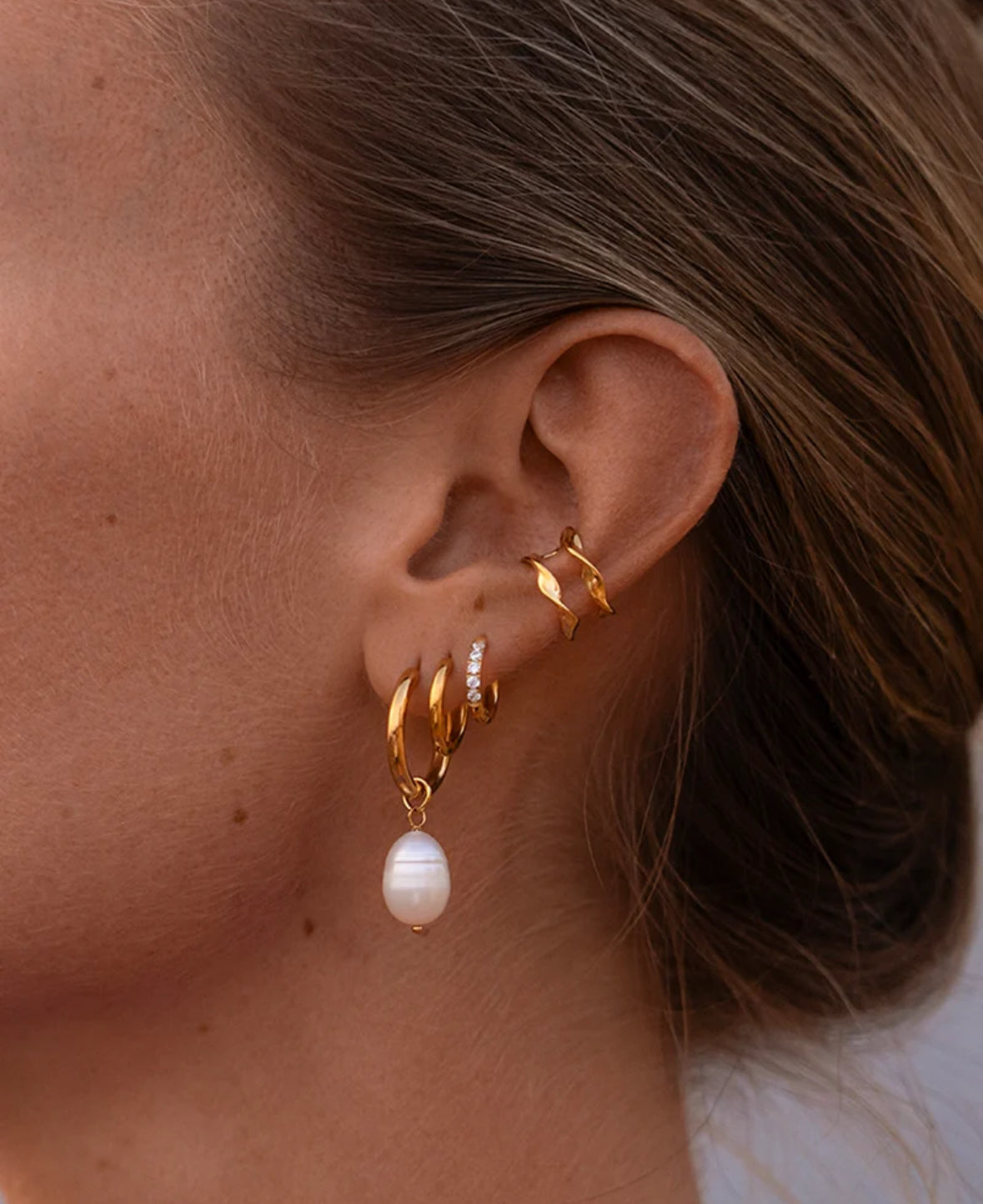 Close-up of an ear wearing gold hoop earrings with a pearl earring.