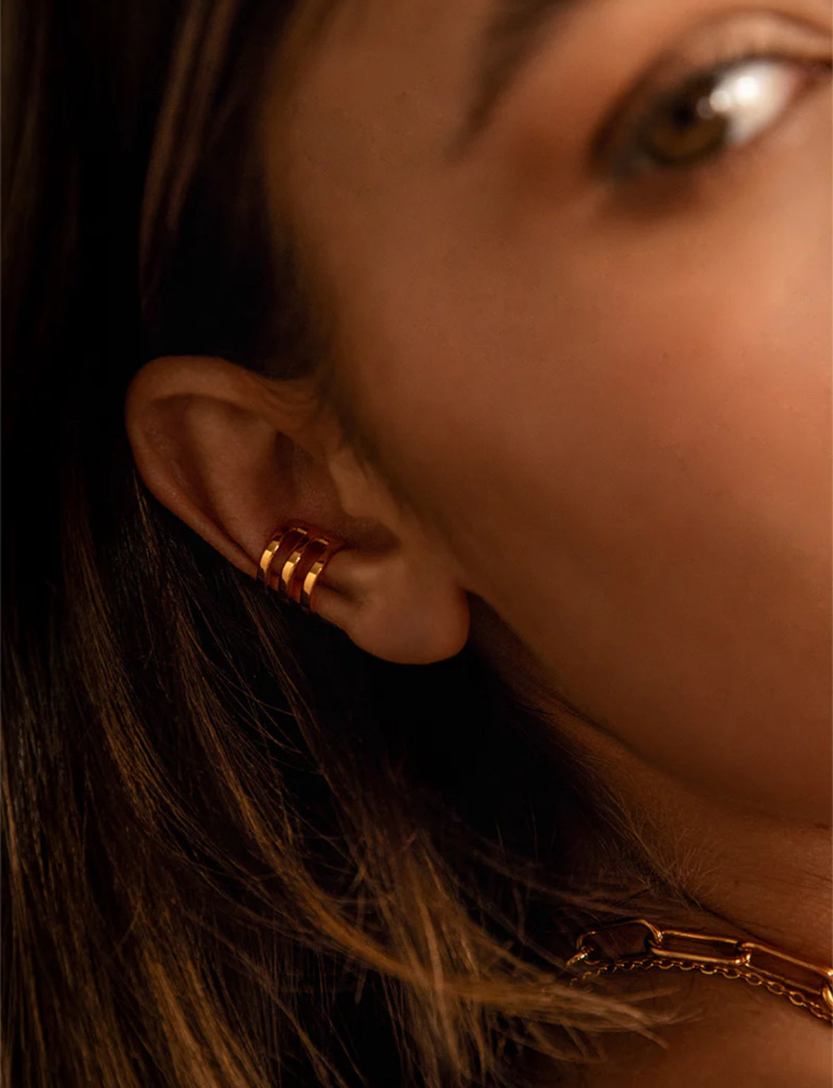 Close-up of a person wearing gold hoop earrings with a blurred background