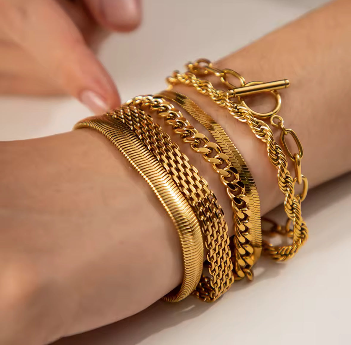 Gold bracelets on a wrist with a neutral background