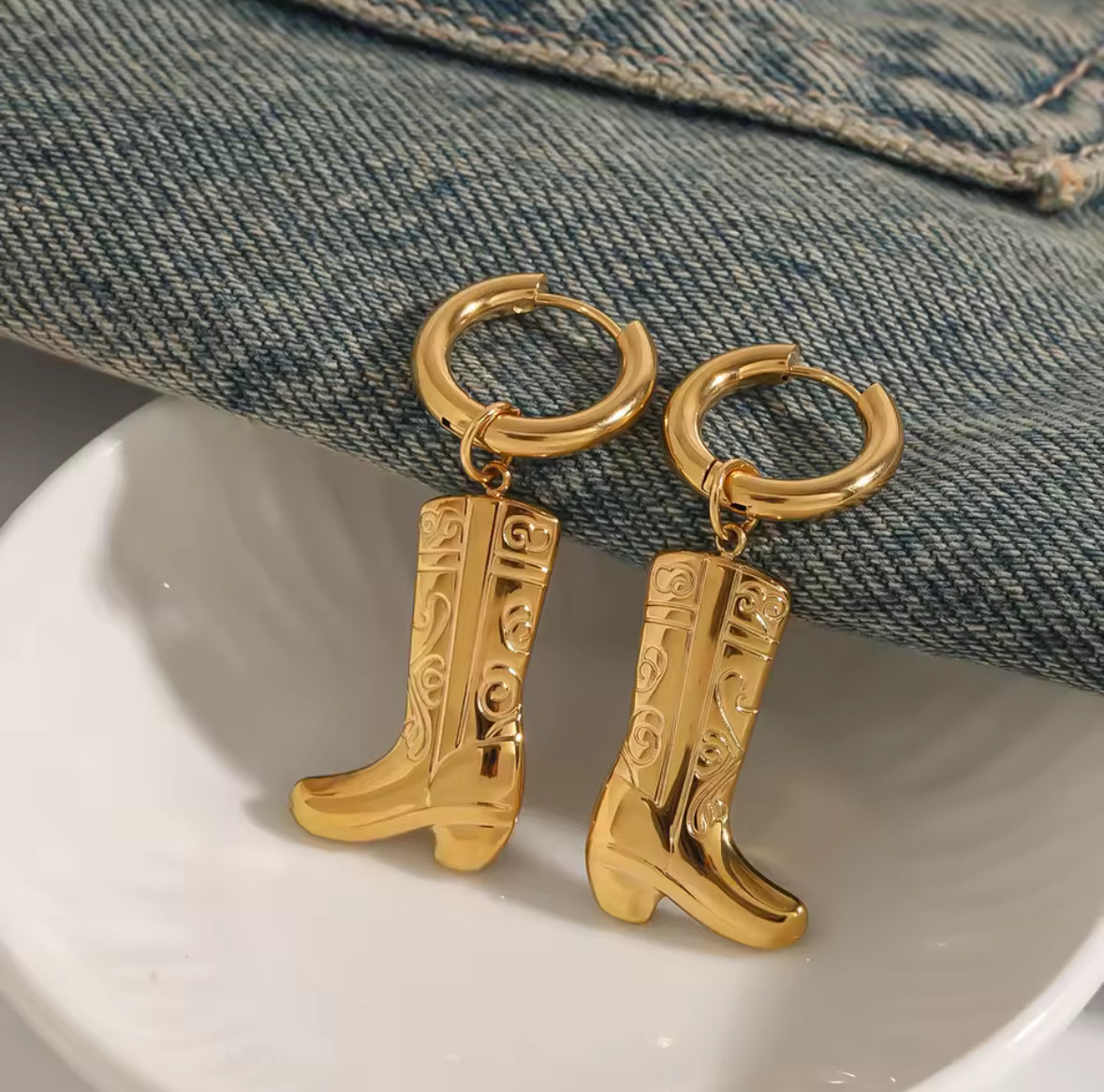 Gold cowboy boot earrings on a white dish with denim background
