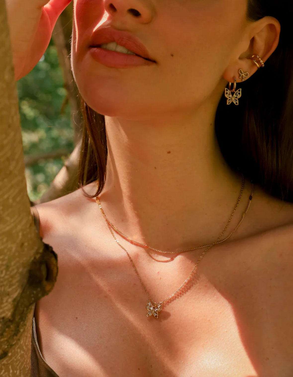 Close-up of a person wearing a necklace and earrings with a blurred natural background
