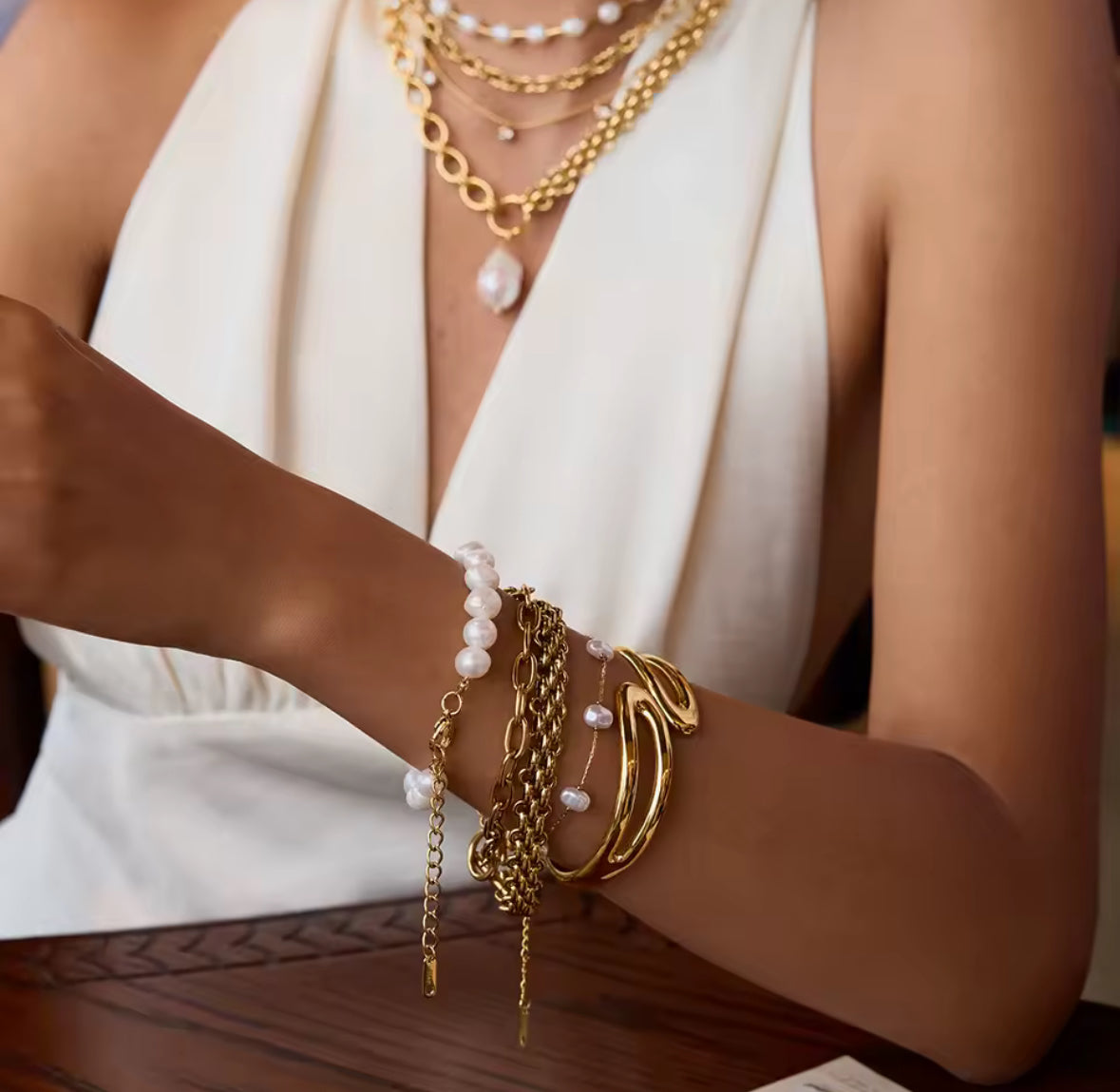 Close-up of a person's arm wearing multiple gold and pearl bracelets and necklaces.