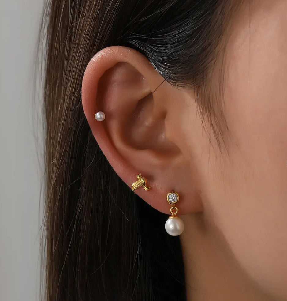 A pair of gold-plated stud earrings with a white pearl-like bead and a yellow gold-plated band in ear