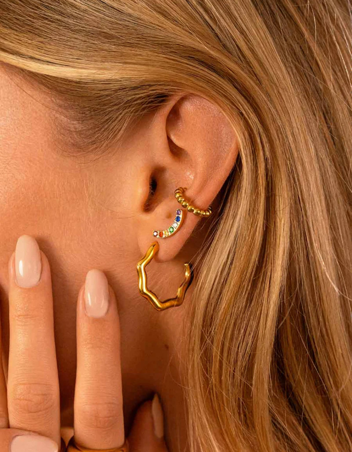 Close-up of a person wearing gold hoop earrings with colorful beads.