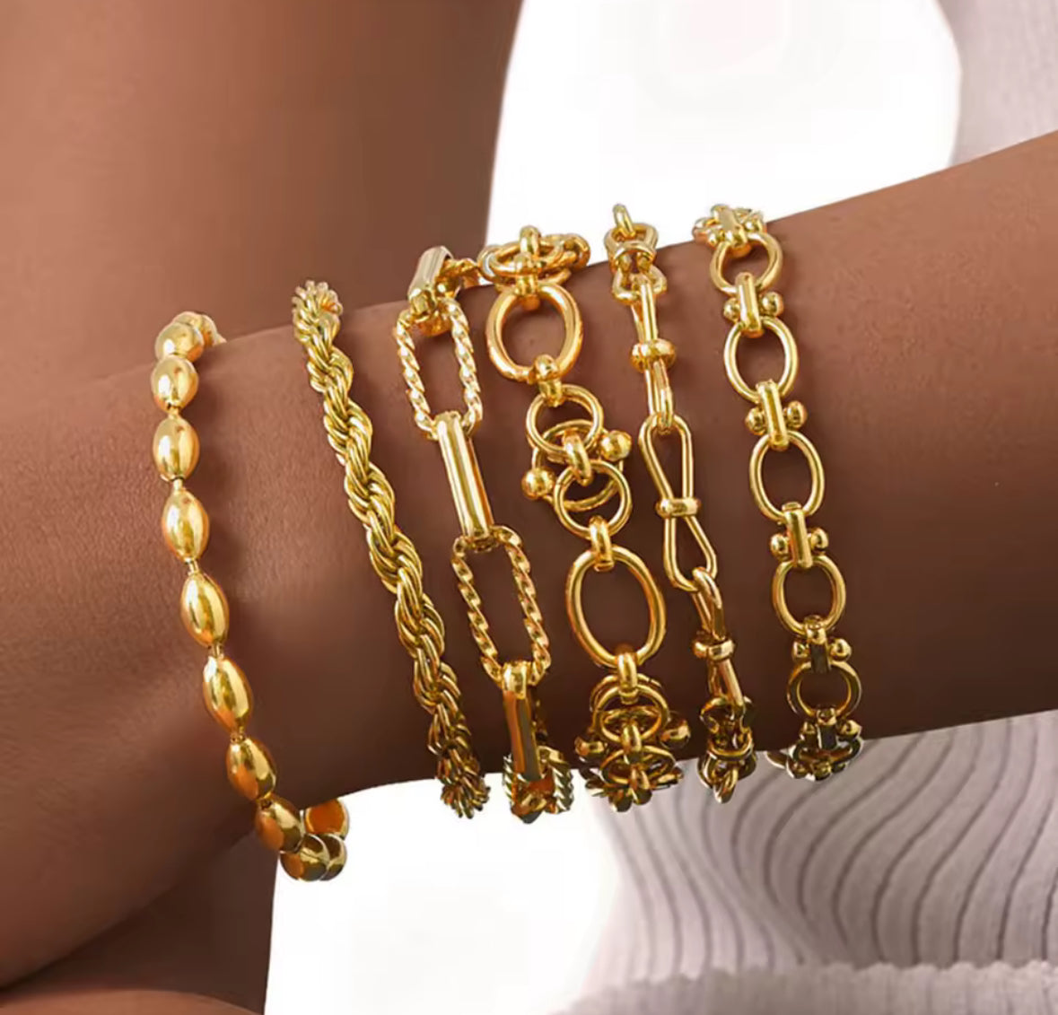 Gold bracelets on a wrist with a neutral background