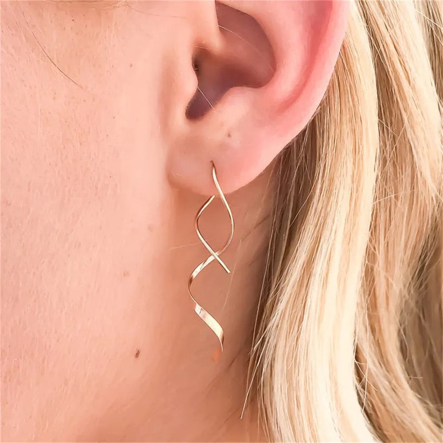 A pair of gold-colored stainless steel earrings with a geometric pattern in ear
