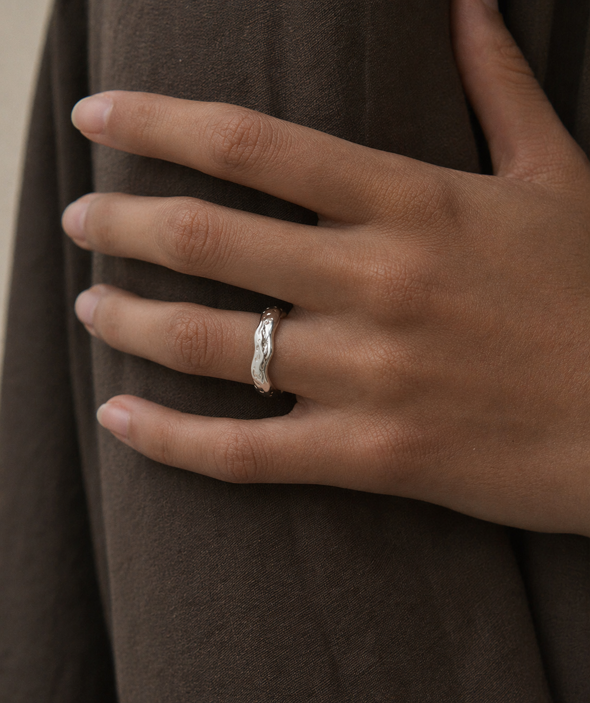 Hand wearing a silver ring with a brown fabric background