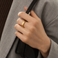 Hand holding a black handbag with a gold ring, wearing a gray suit.